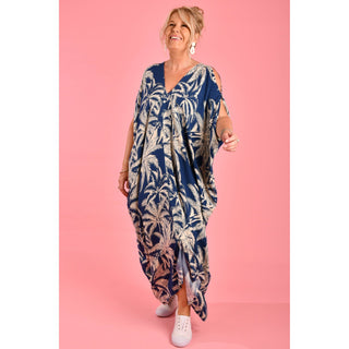 Introducing the Cushla Dress, a stunning Kaftan maxi dress in a timeless Navy hue featuring a charming palm Tree print with cream tones. This dress boasts unique button details on the shoulder and arm, creating stylish openings that enhance its batwing sleeves for a flowing design. 