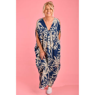 Introducing the Cushla Dress, a stunning Kaftan maxi dress in a timeless Navy hue featuring a charming palm Tree print with cream tones. This dress boasts unique button details on the shoulder and arm, creating stylish openings that enhance its batwing sleeves for a flowing design. 