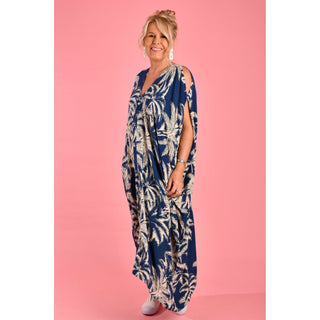 Introducing the Cushla Dress, a stunning Kaftan maxi dress in a timeless Navy hue featuring a charming palm Tree print with cream tones. This dress boasts unique button details on the shoulder and arm, creating stylish openings that enhance its batwing sleeves for a flowing design. 