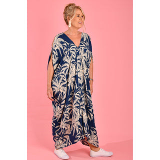 Introducing the Cushla Dress, a stunning Kaftan maxi dress in a timeless Navy hue featuring a charming palm Tree print with cream tones. This dress boasts unique button details on the shoulder and arm, creating stylish openings that enhance its batwing sleeves for a flowing design. 