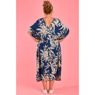 Introducing the Cushla Dress, a stunning Kaftan maxi dress in a timeless Navy hue featuring a charming palm Tree print with cream tones. This dress boasts unique button details on the shoulder and arm, creating stylish openings that enhance its batwing sleeves for a flowing design. 